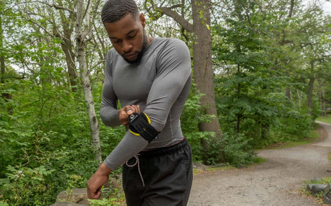 Person adjusting an M-Brace elbow support outdoors / Personne ajustant une orthèse de coude M-Brace à l’extérieur