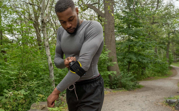 Person adjusting an M-Brace elbow support outdoors / Personne ajustant une orthèse de coude M-Brace à l’extérieur