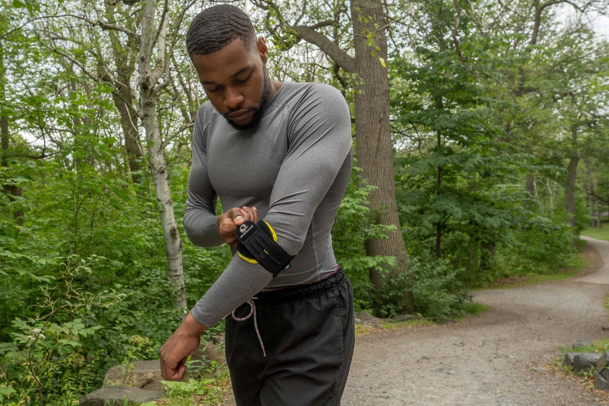 Person adjusting an M-Brace elbow support outdoors / Personne ajustant une orthèse de coude M-Brace à l’extérieur