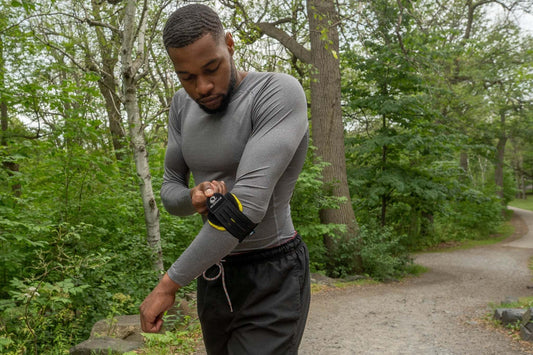 Person adjusting an M-Brace elbow support outdoors / Personne ajustant une orthèse de coude M-Brace à l’extérieur