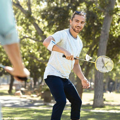 Man playing badminton wearing EpiPoint Elbow Brace in a park setting.